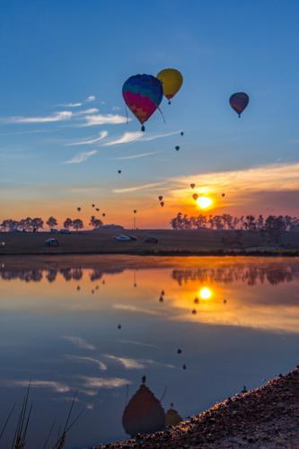 Hot air balloons reflected over lake on a colourful sunrise
