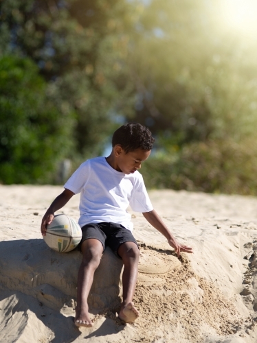 Indigenous boy playing with ball on a sand ledge at beach