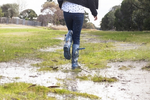 Kid splashing in puddles in gumboots on a rainy winter day.