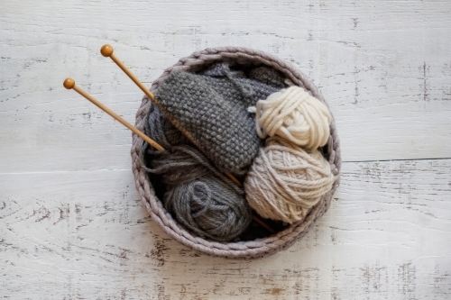 Knitting in grey woven basket with wooden knitting needles and grey and cream wool