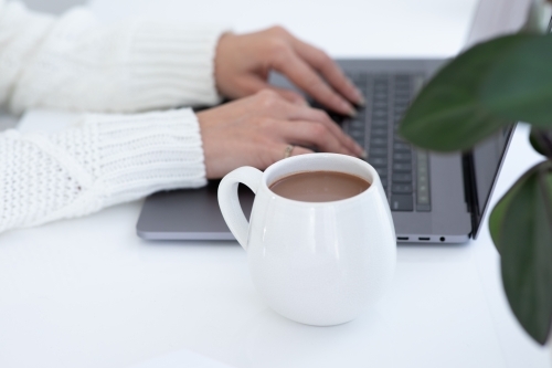 lady's hands typing on laptop with white hug mug in the foreground