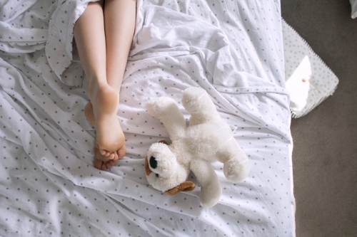 Legs and feet of a child laying in a messy bed with a teddy
