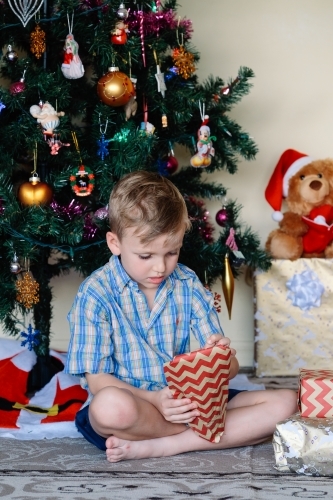 Little boy opening a gift on Christmas day next to the Christmas tree