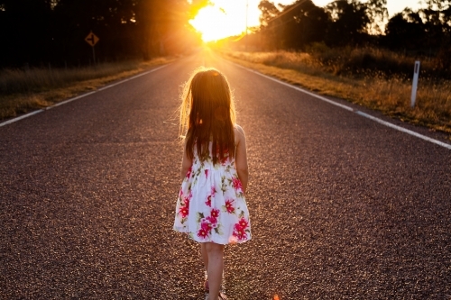 Little girl walking down road towards sunset in glowing golden light
