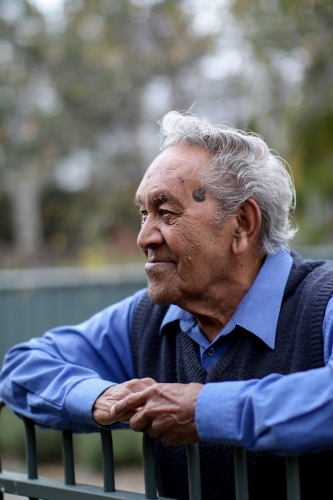 Male Aboriginal elder smiling and leaning against fence