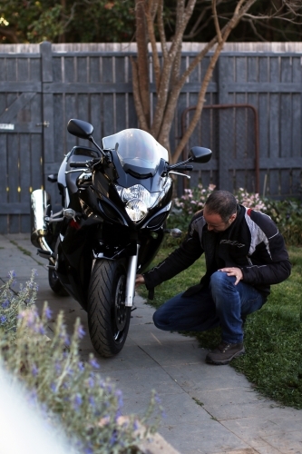 Man crouching next to motorbike in garden