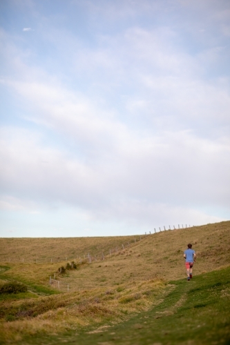 Man Running Uphill From Distance Under Blue Sky