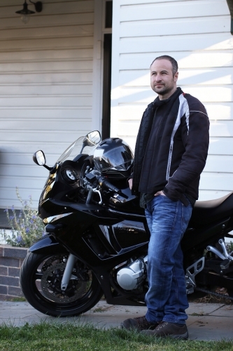 Man standing with motorbike outside of house