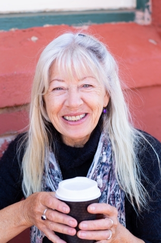 mature lady with long hair holding takeaway coffee cup with both hands