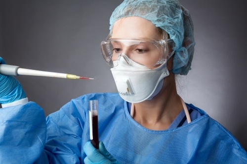 Medical pathologist or research scientist wearing protective PPE analysing sample