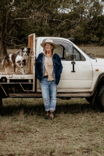 Mid fifties woman with eyes closed stands next to ute on the farm.