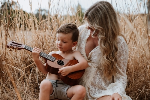 Mother and son sitting close together outside in field with small guitar