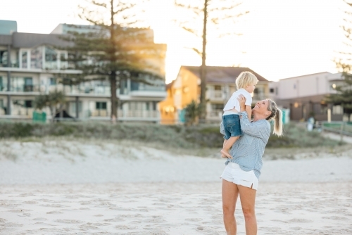 Mother lifting toddler son, playing on Gold Coast beach