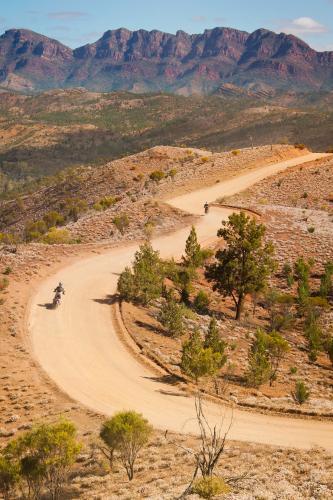 Motorbikes riding on a winding dirt road that follows a mountain spur