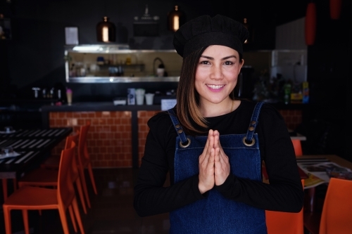 Multicultural Asian small business owner greeting in front of Thai restaurant