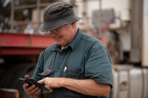 older worker wearing bucket hat using smartphone near machinery