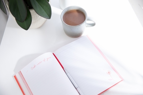 Open journal on a white desk with a hot beverage in a mug in morning light