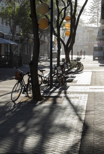 Paved urban mall in early morning light with trees, shadows, parked bicycles and distant pedestrians
