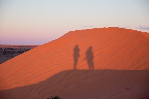 People shadows on red sand dune