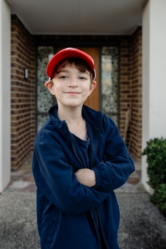 Portrait of a happy, young Australian boy wearing a red cap standing outside his home