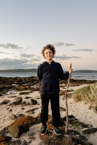 Portrait of a young boy posing with a walking stick on a beach at sunset