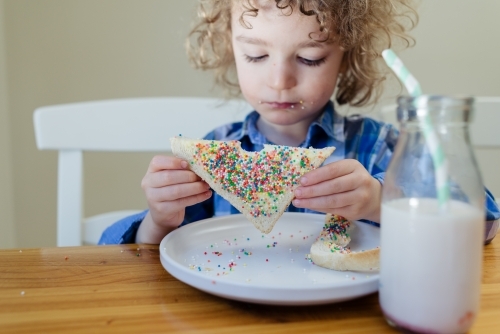 Portrait of a young boy with blond curly hair sitting at the table eating fairy bread