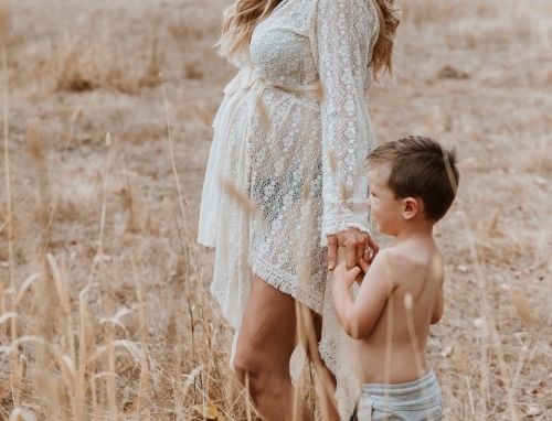 Pregnant mother walking with son through brown grass