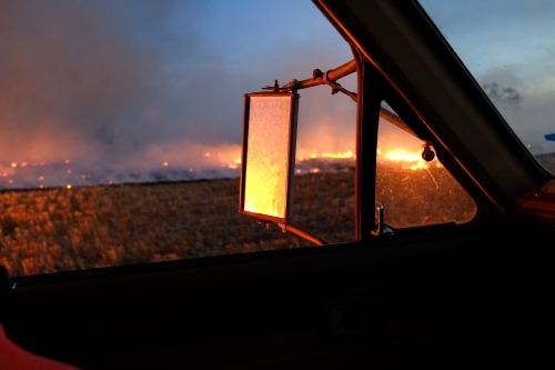 Prescribed burn off on the farm showing flames in the night light reflected in ute side mirror