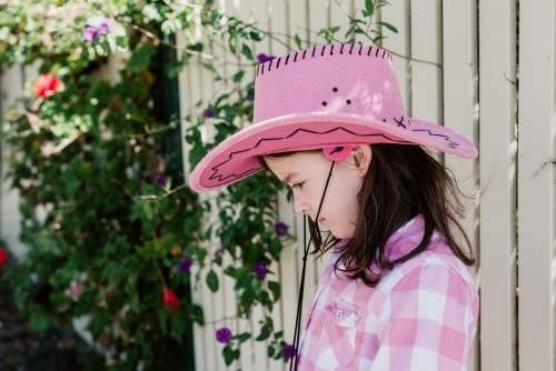 Profile of happy young girl dressed up as a cowgirl wearing a pink akubra hat and pink check shirt