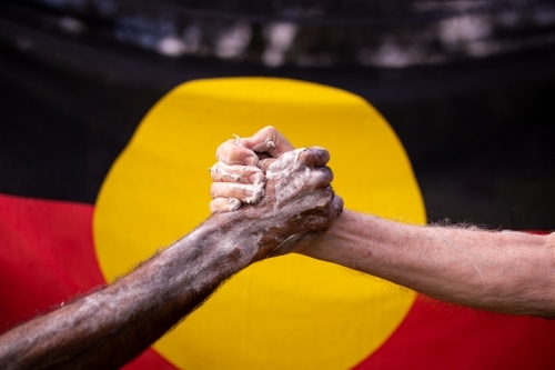 Reconciliation concept - indigenous elders hand clasped with white man's in front of aboriginal flag