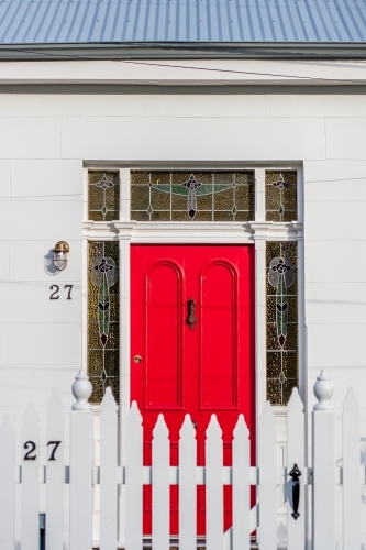 Red front door with white picket fence in urban streetscape