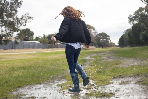 Red haired girl splashing in puddles in gumboots on a rainy winter day.
