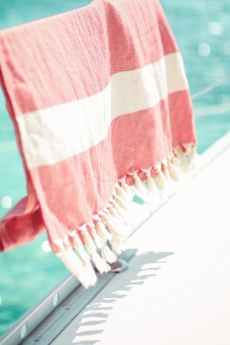 Red turkish towel hanging on wire railing of boat on the water