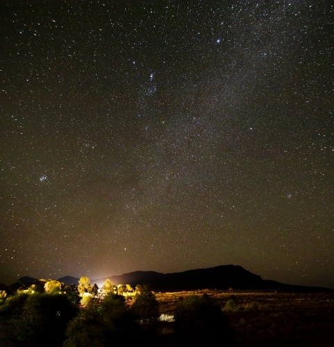 remote building and trees lit up under starry sky with hill in background