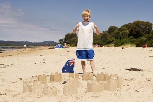 Sandcastle with flag and boy with thumbs up