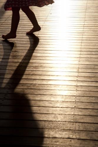 Silhouette and shadow of a young girl dancing on a sunlit deck