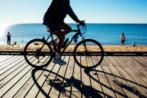 Silhouette of a cyclist riding along a timber boardwalk by the beach at Redcliffe, Queensland.