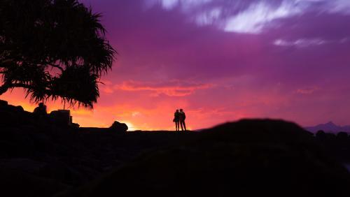 Silhouette of couple and tree with colourful coastal sunset in background