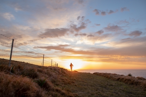 Silhouette of Man in Distance Running Towards Sunrise