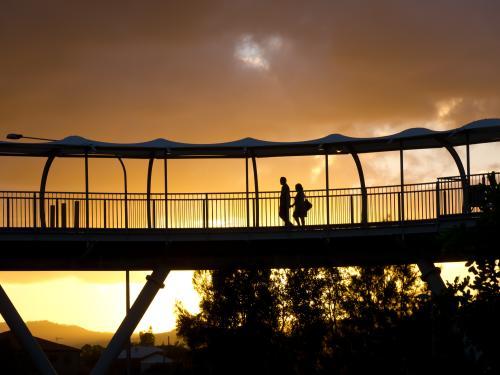 Silhouetted man and woman walking across an overpass at sunset