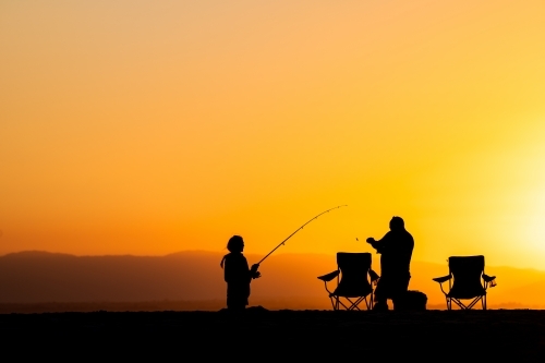 silhouettes of people fishing on the beach at sunset