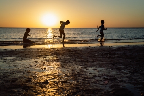 Silhouettes of three children playing on the beach at sunset