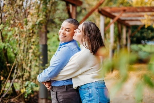 smiling lgbtqi couple hugging and kissing on the cheek
