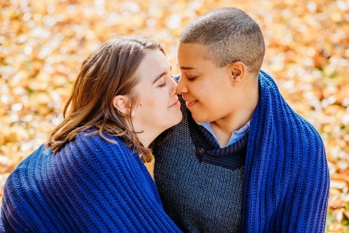 smiling lgbtqi couple looking at each other outside with blue blanket wrapped around them