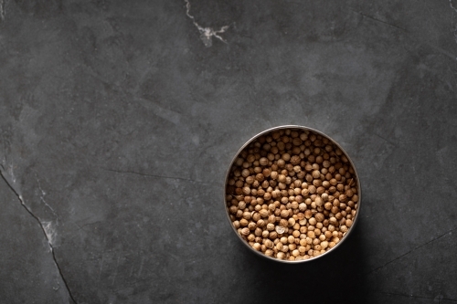 Spice tin of coriander seeds on dark marble background