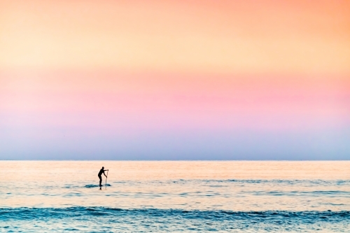 Stand up paddler in the ocean at dawn