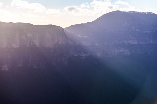 Sunrise beams of light shine over the sandstone cliffs of the Gross valley in the Blue Mountains NP