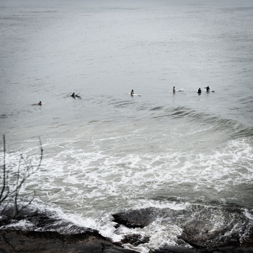 surfers out to sea waiting for a wave near rocky shoreline