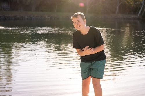 Teen boy laughing at water's edge in golden afternoon light