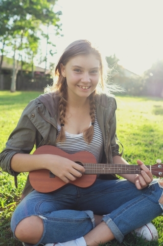 Teenage girl playing ukulele in the park